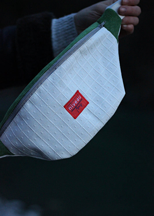 Banane Tchikita en toile beige et velours vert, sangle blanche, zip gris, logo sur le devant.