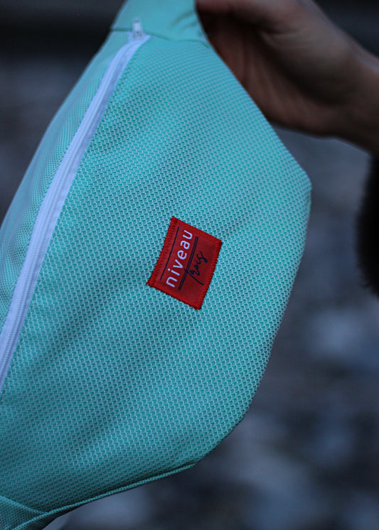 Banane Tchikita en toile déperlante turquoise à motifs, sangle blanche, zip blanc, logo sur le devant.