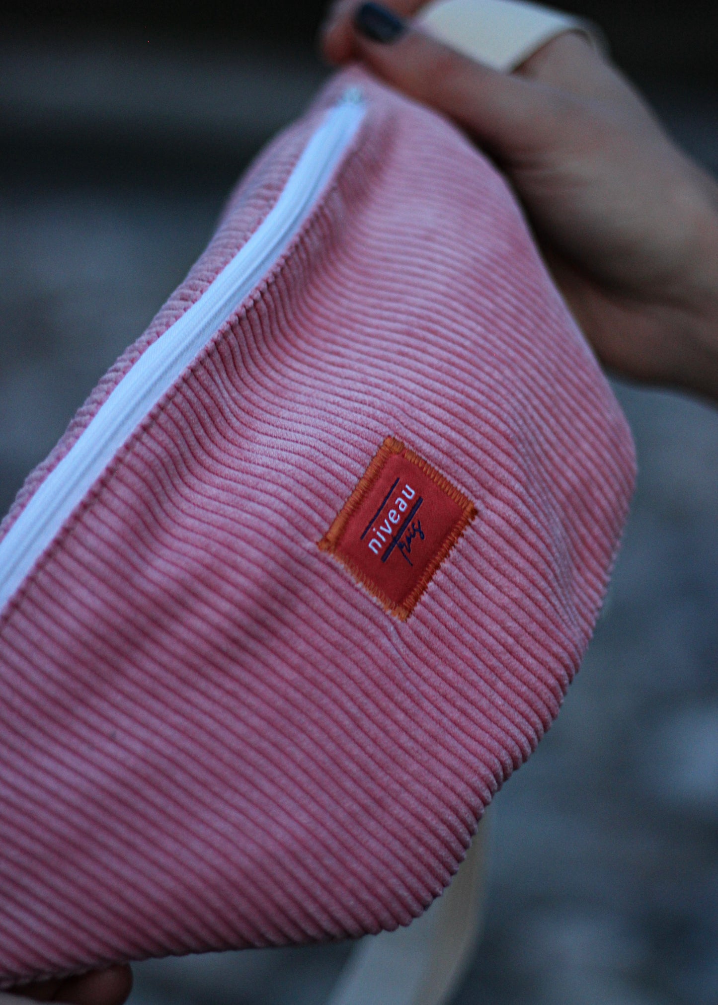Banane Tchikita en velour côtelé rose, sangle blanche, zip blanc, logo sur le devant.