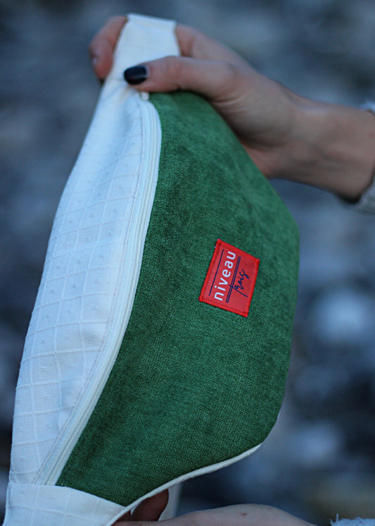 Banane en velours vert et toile beige, zip blanc, sangle blanche, logo devant, zoom sur le logo.