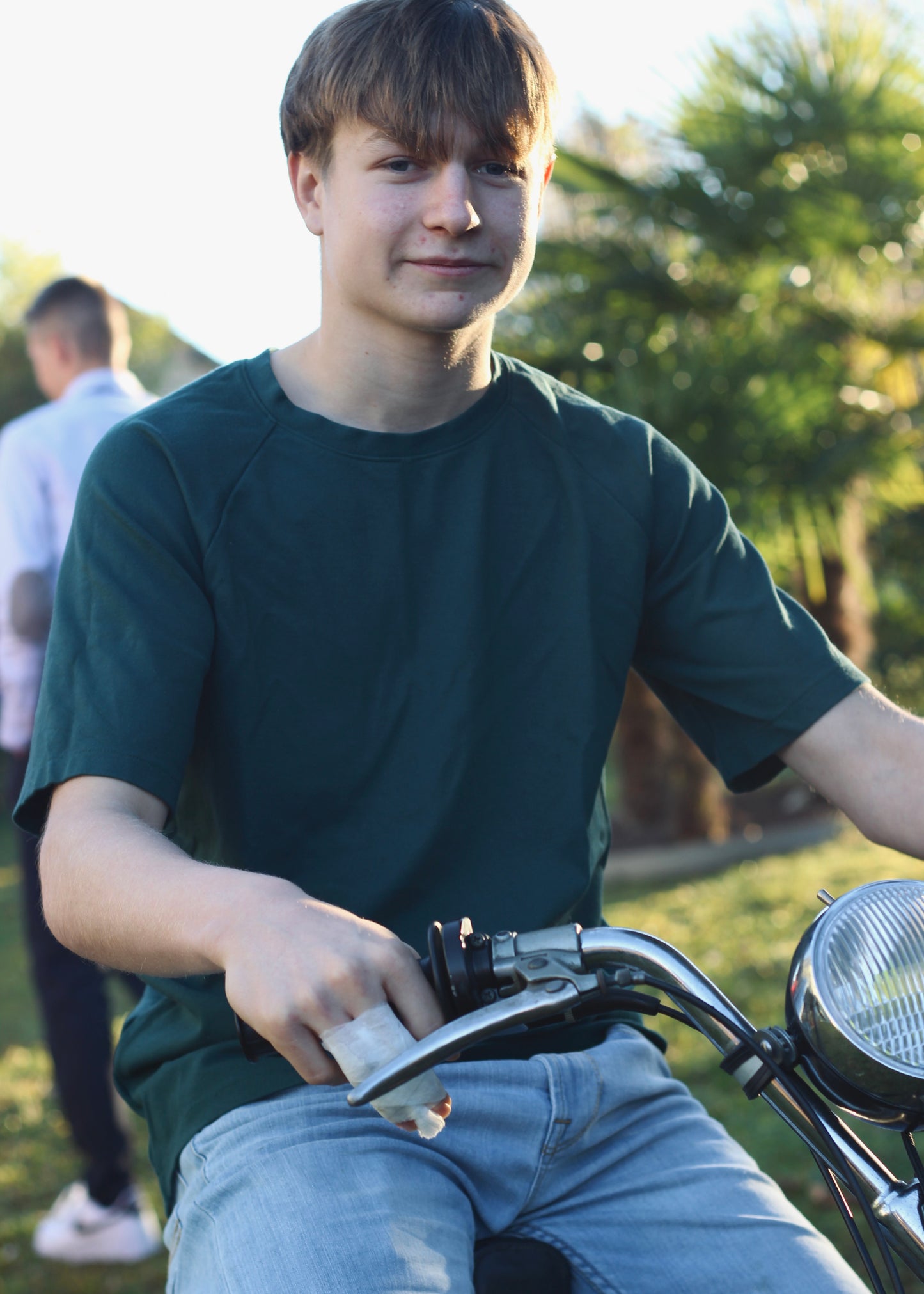 Jeune homme portant le t-shirt Dama vert, assis sur une mobylette.