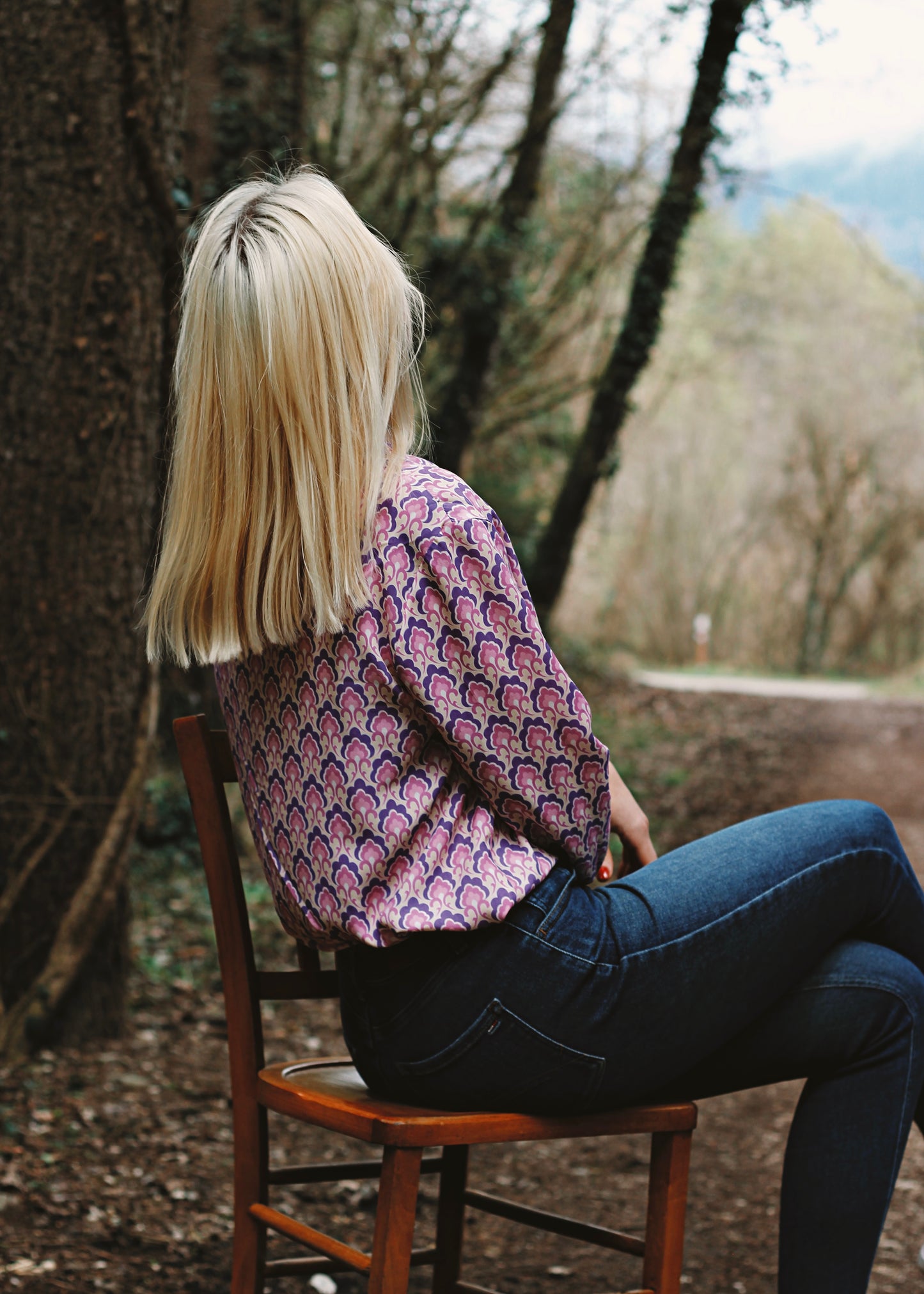 Femme portant le chemisier Iris lila, assise sur une chaise, en forêt