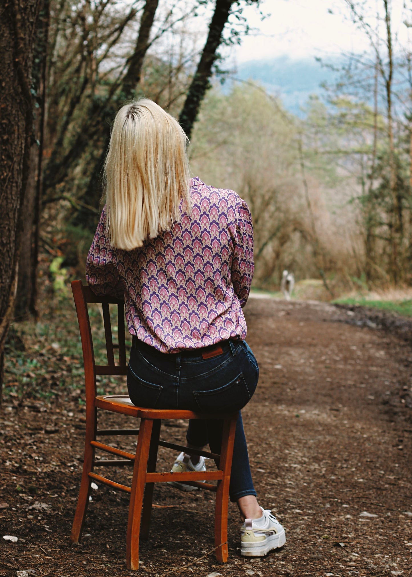 Femme portant le chemisier Iris lila, assise sur une chaise, en forêt