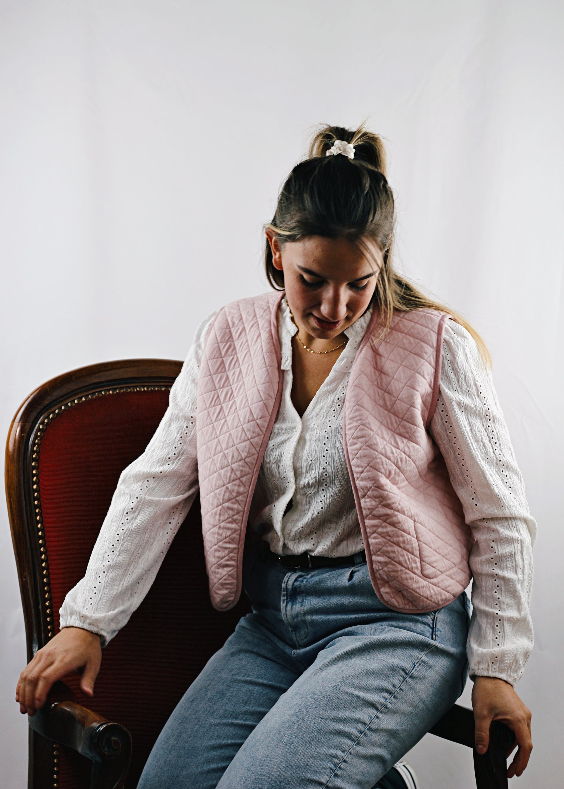 Gilet Alca en tissu molletonné rose réversible, jeune femme assise sur le fauteuil, regardant vers le bas.