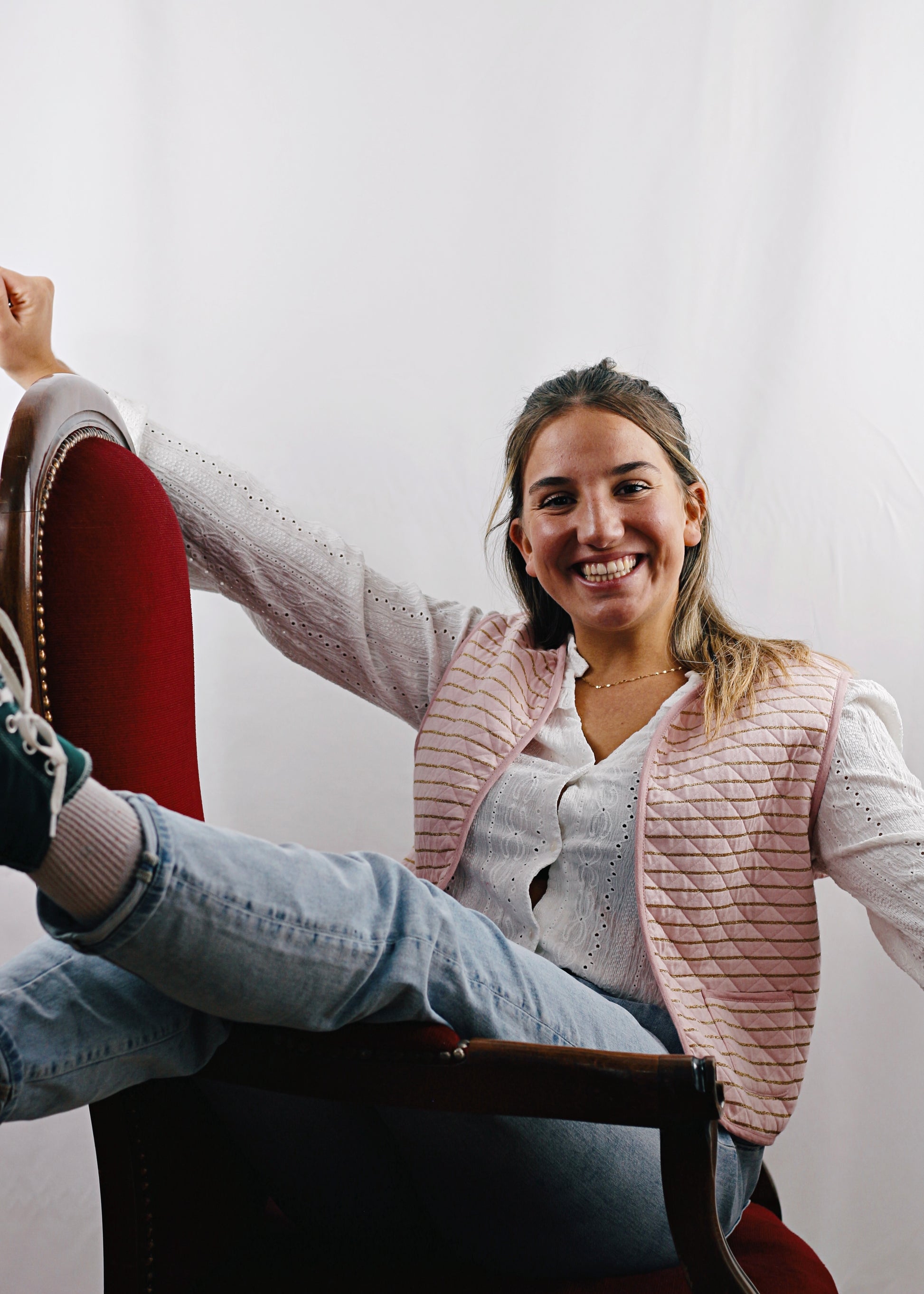 Gilet Alca en tissu molletonné rose réversible, jeune femme assise sur le fauteuil, les bras ouverts.