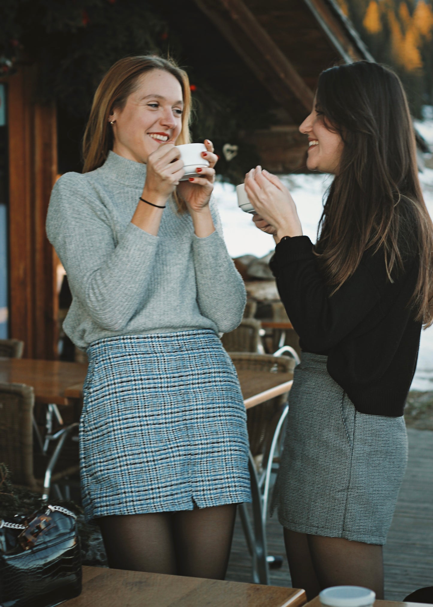 2 amies dans un café en montagne, en jupe-short et pull, ambiance hivernale au soleil couchant.