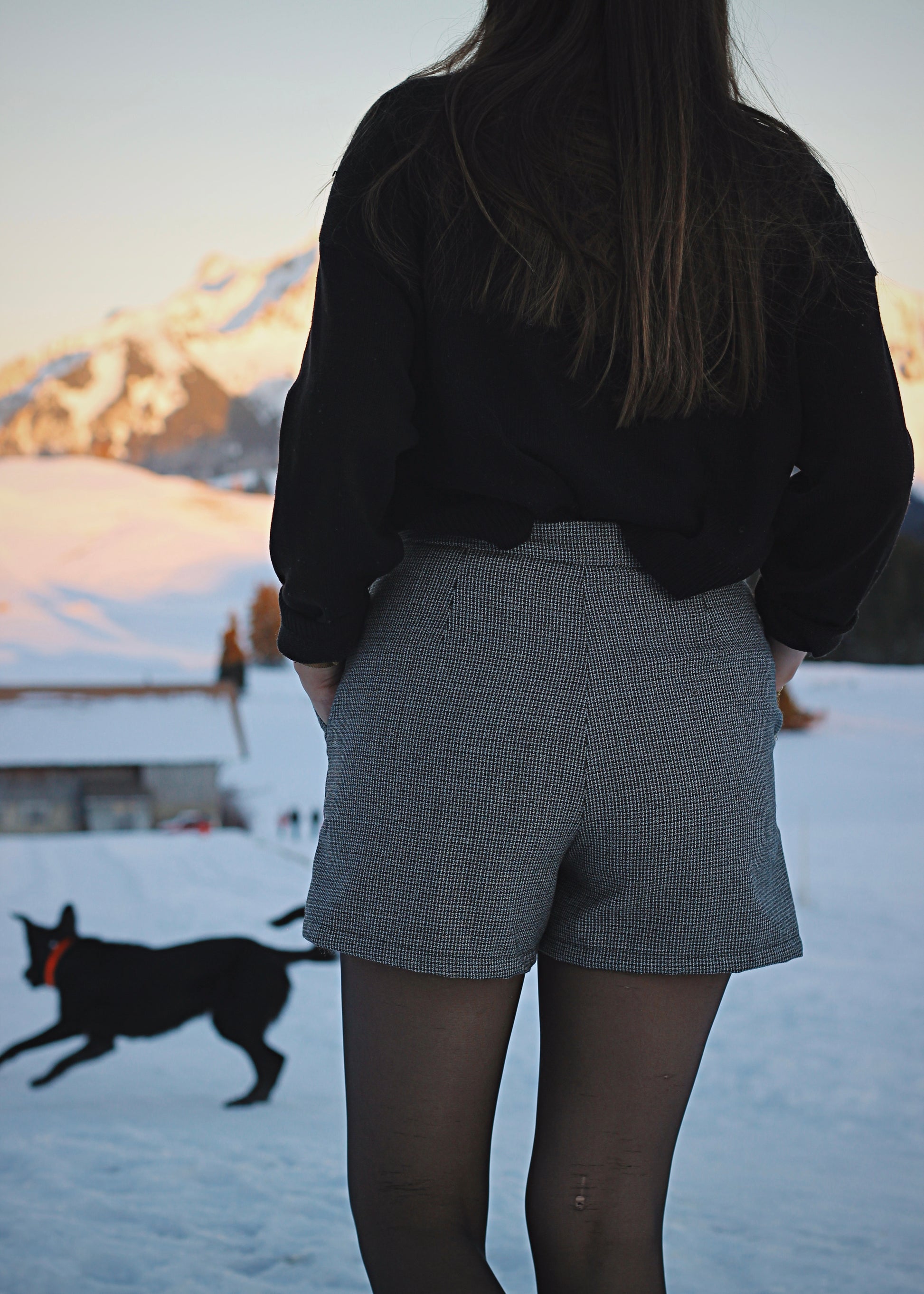 Jupe-short dans la neige, ambiance hivernale au soleil couchant, zoom sur la jupe de dos, chien en arrière-plan.