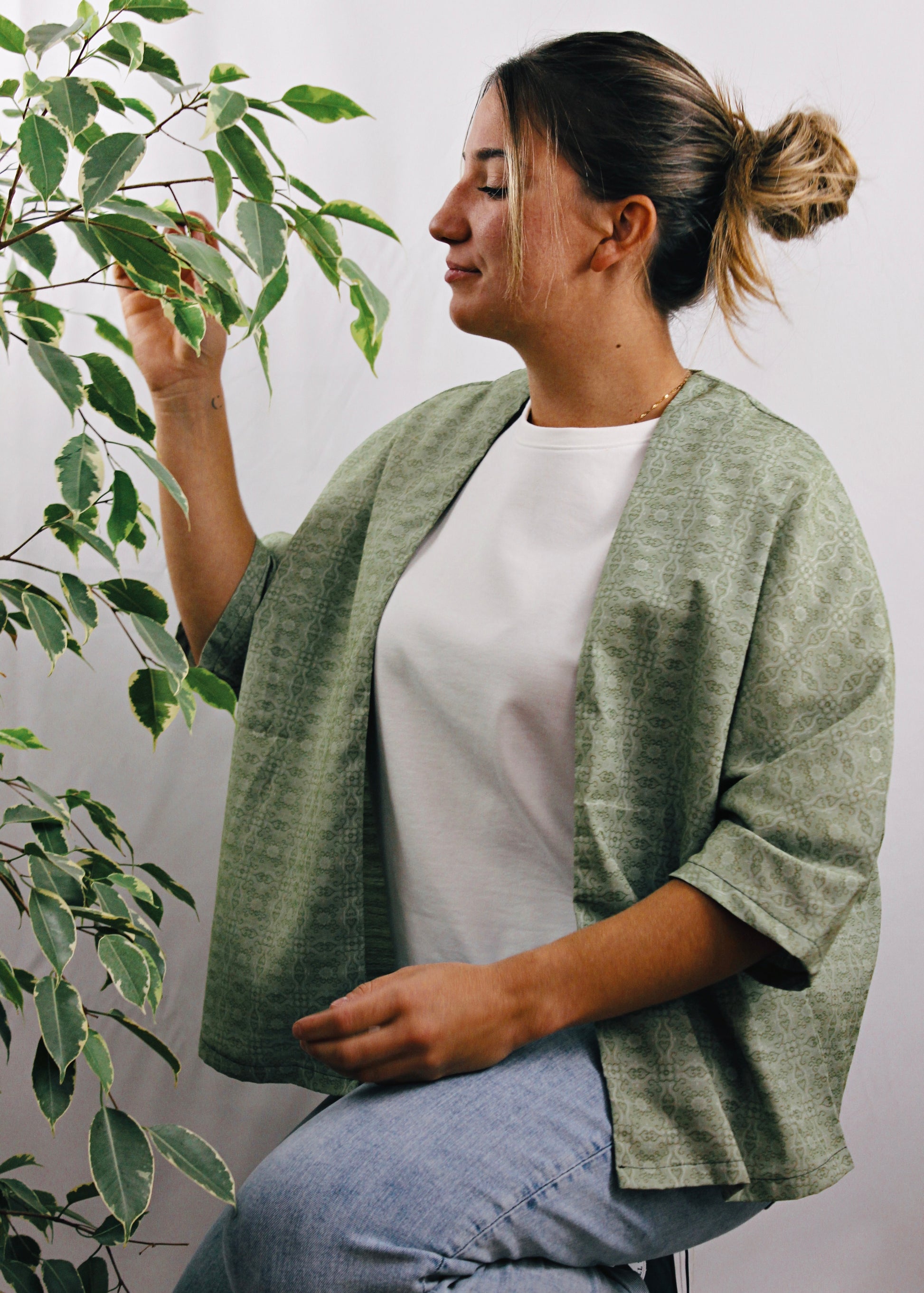 Kimono Sakura, jeune femme assise sentant les plantes, tissu vert à motifs.