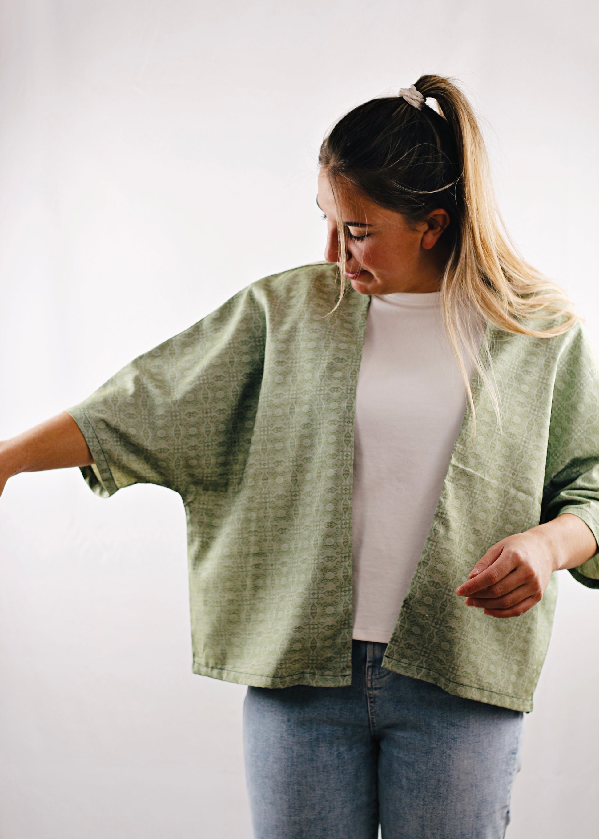 Kimono Sakura, vue de face, jeune femme reagardant sa manche, tissu vert à motifs.