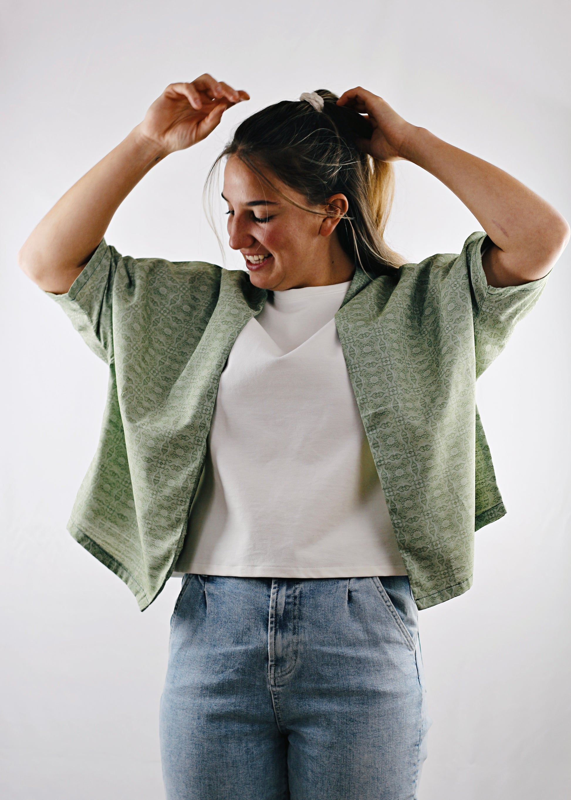 Kimono Sakura, vue de face, jeune femme se coiffant, tissu vert à motifs.