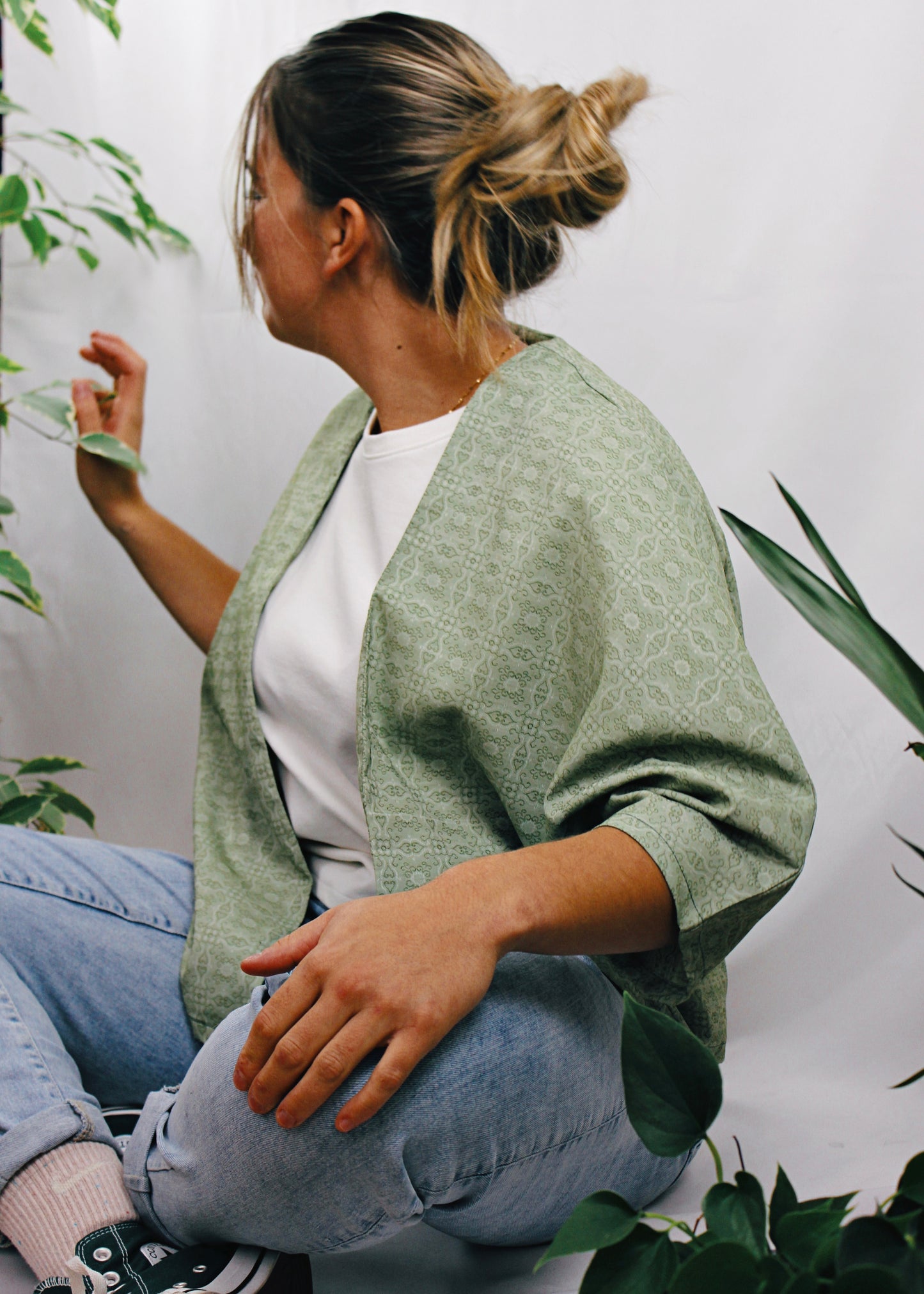 Kimono Sakura, jeune femme assise regardant les plantes, tissu vert à motifs.