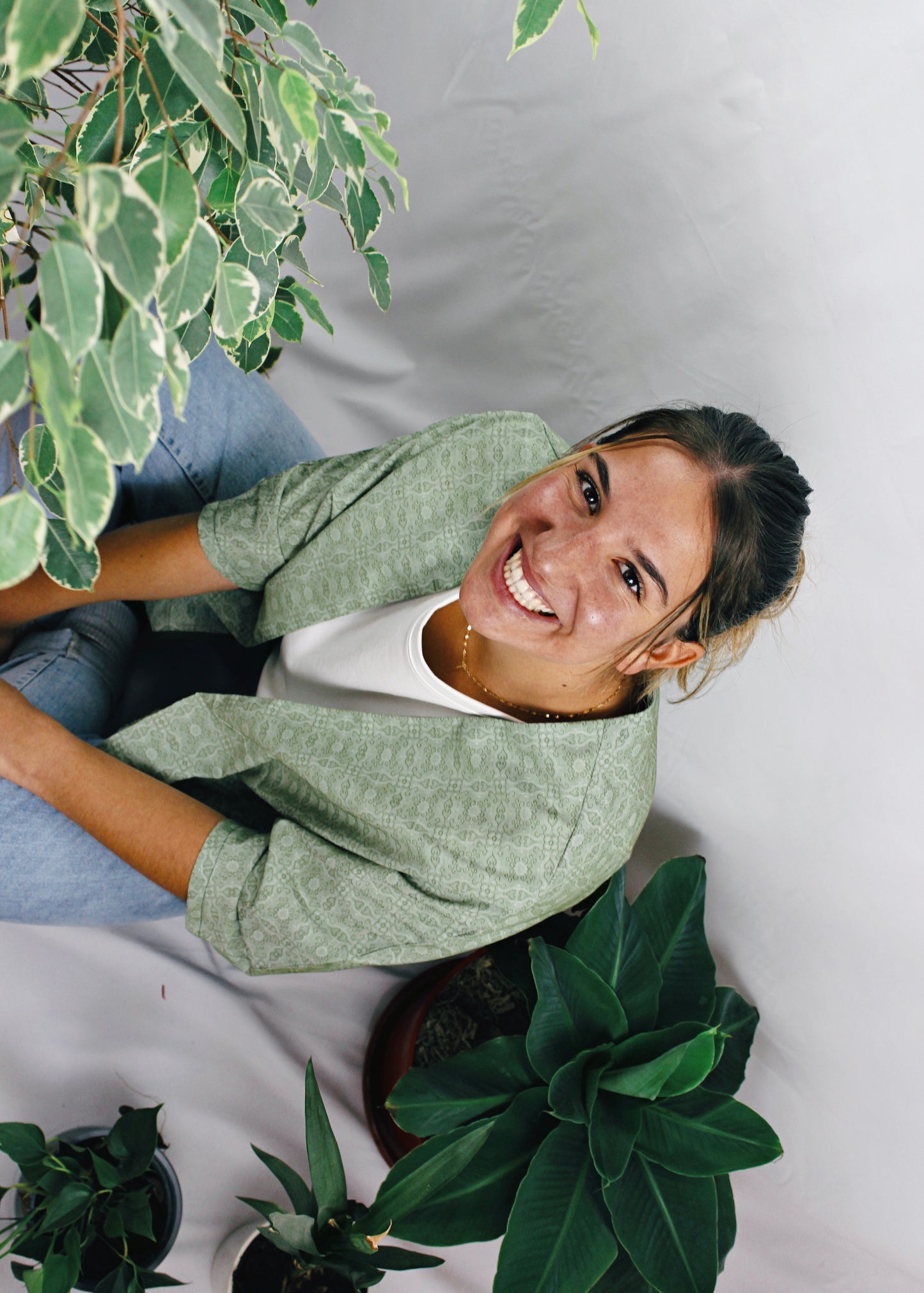 Kimono Sakura, jeune femme assise au milieu des plantes, souriante, tissu vert à motifs.