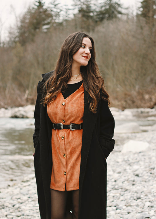 Femme portant la robe Nyssa brique ceinturée, au bord de la rivière.